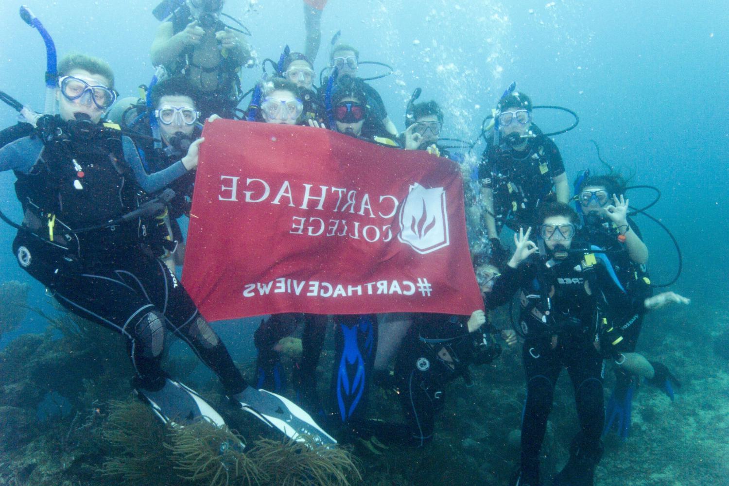 学生们手持<a href='http://7uuy6.00766.net'>全球十大赌钱排行app</a>旗帜，在j学期洪都拉斯游学之旅中潜水.